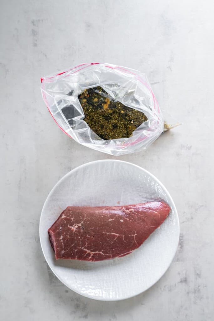 Marinade ingredients in a zip top bag. London Broil on a white plate.