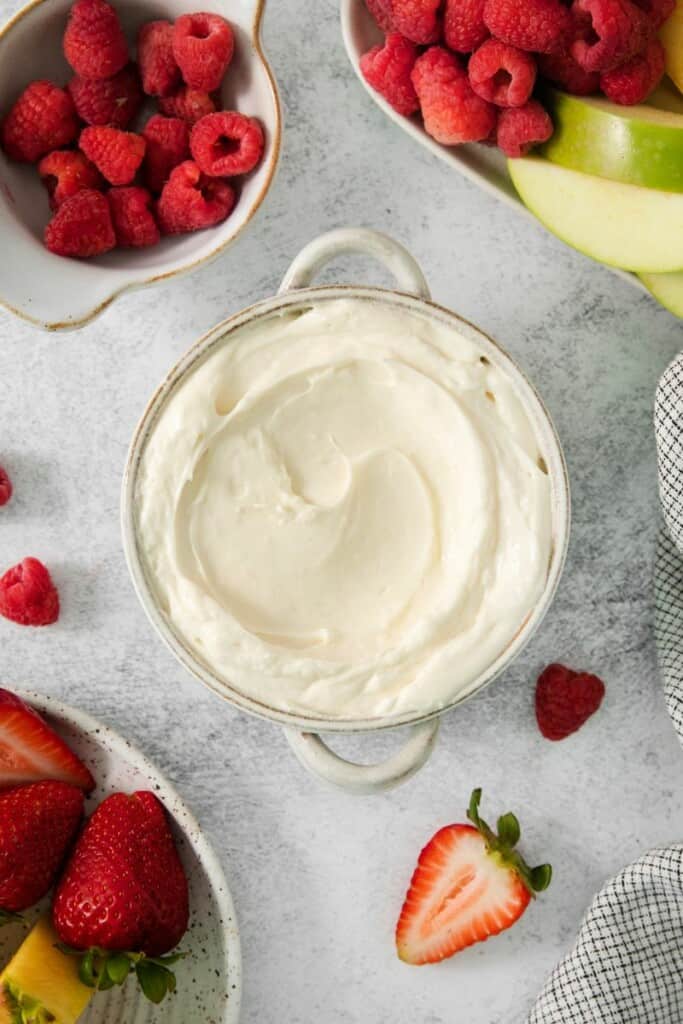 Prepared marshmallow dip for fruit on a small bowl surrounded by strawberries.