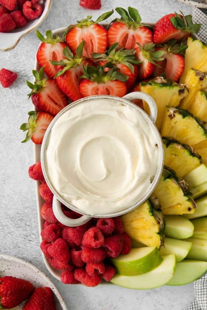 A bowl of marshmallow dip for fruit surrounded by sliced fruit.