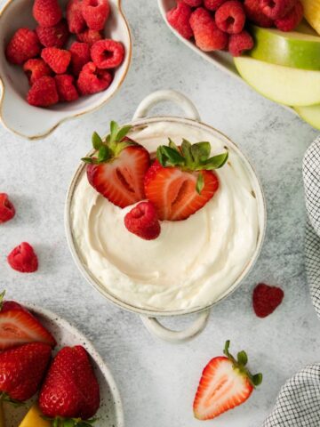 A bowl of marshmallow dip for fruit topped with strawberries.