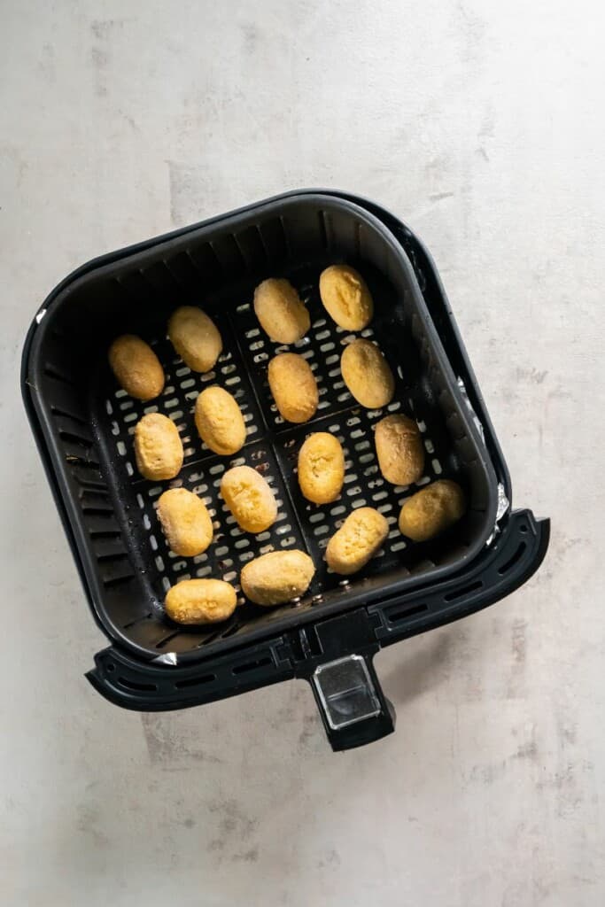 Mini corn dogs in an even layer of a black air fryer basket.