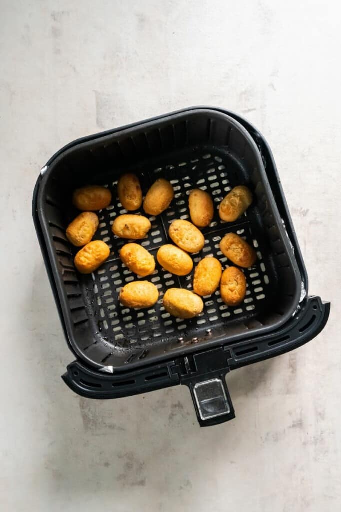 Cooked mini corn dogs in a black air fryer basket.
