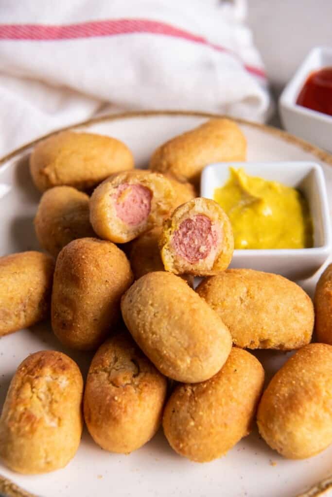 A mini corn dog sliced in half resting on a platter of additional mini corn dogs.