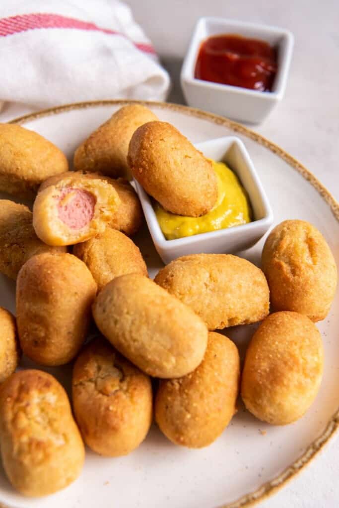 A mini corn dog dipped in mustard on a platter with additional mini corn dogs.