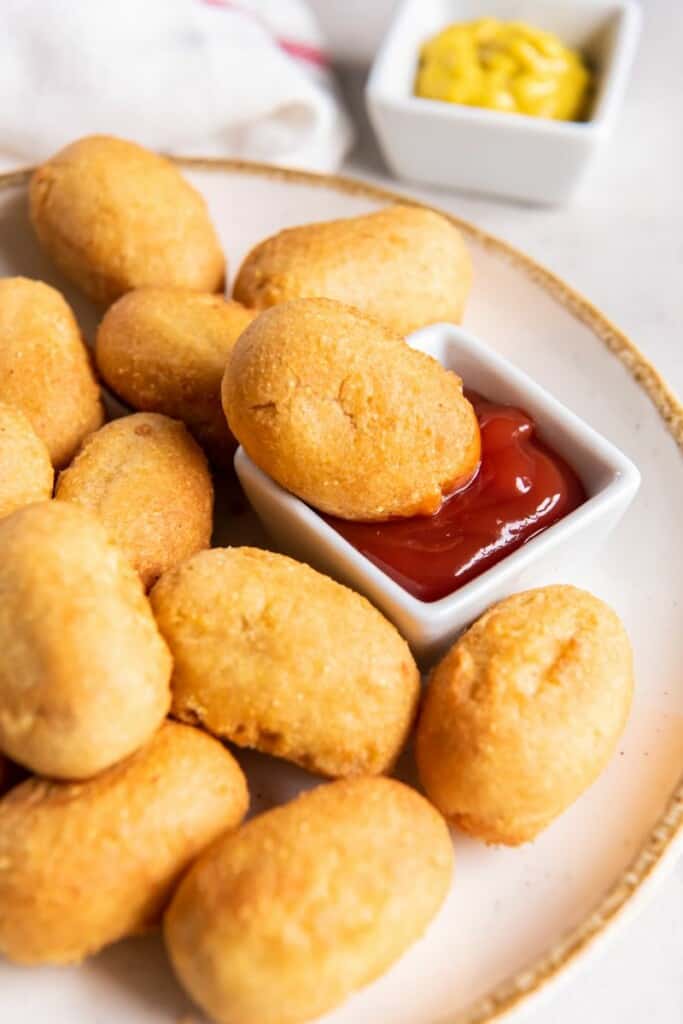 A mini corn dog dipped in ketchup on a platter of additional mini corn dogs.