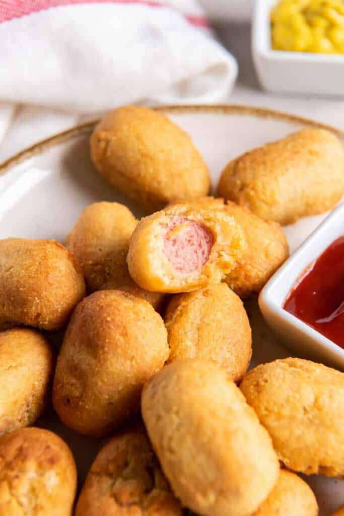 A mini corn dog bit in half on a platter with additional mini corn dogs.