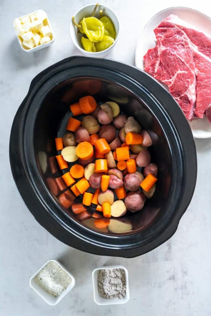 Adding carrots and potatoes to a black slow cooker.