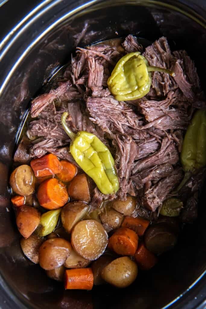 Close up view of prepared Mississippi Pot Roast and vegetables in a black slow cooker.
