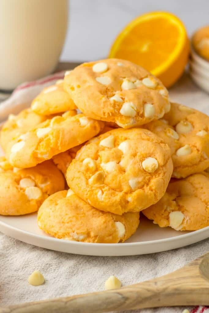 Close up view of orange cookies arranged on an off-white plate with a glass of milk in the background.