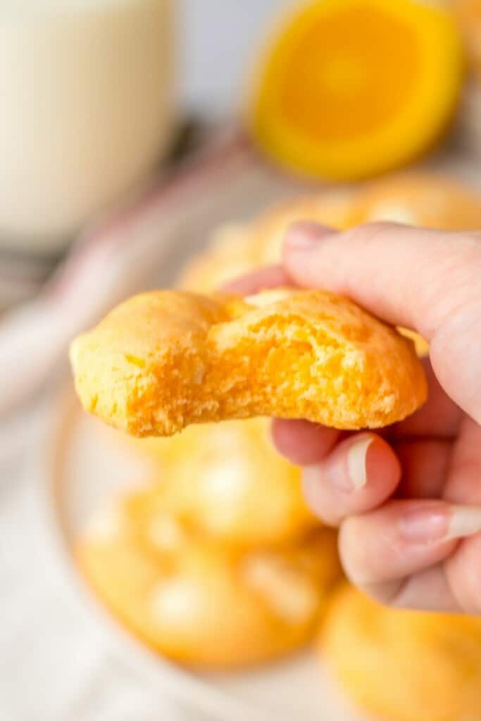 A hand holding an orange cookie with a bite taken out so the center is visible.