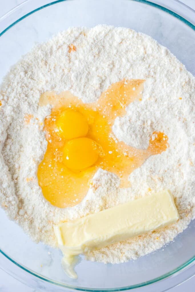 Adding butter and eggs to the dry ingredients for orange cookies in a clear mixing bowl.