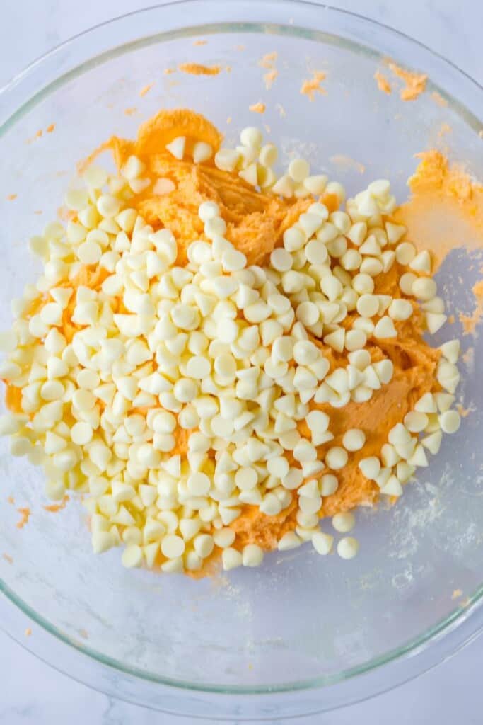 Folding white chocolate chips into cookie batter in a clear mixing bowl.