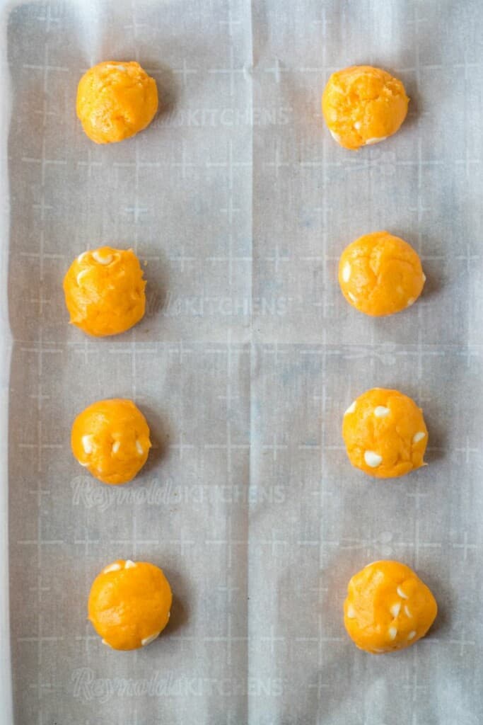 Scooping orange cookie dough into balls and placing them on a parchment lined baking sheet.