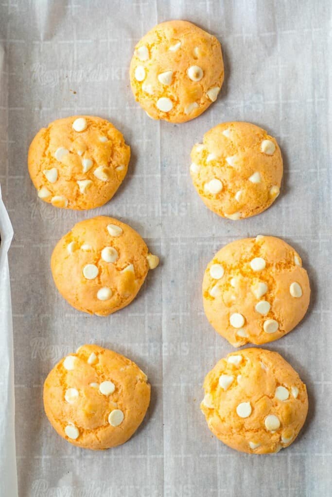 Seven baked orange cookies on a parchment lined baking sheet.