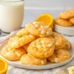 Baked orange cookies on a white plate with a glass of milk in the background.