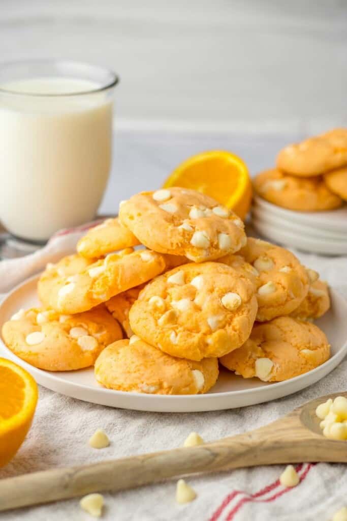 Baked orange cookies on a white plate with a glass of milk in the background.