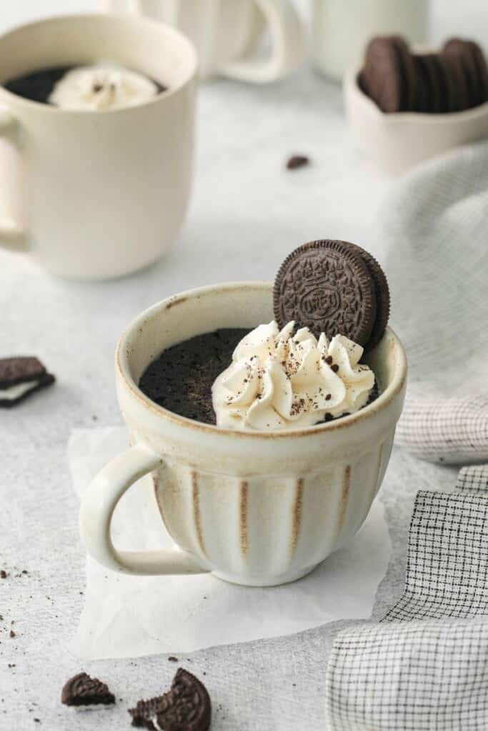 A prepared oreo cake in a mug topped with whipped cream and an oreo.