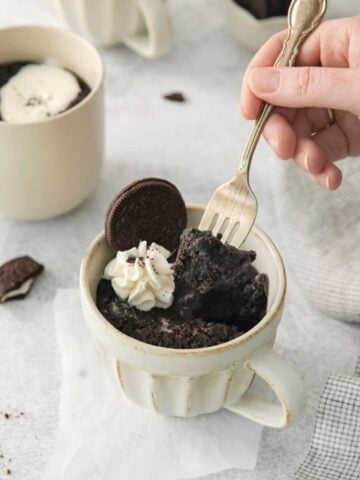 A fork lifting a bite of oreo cake out of a mug.
