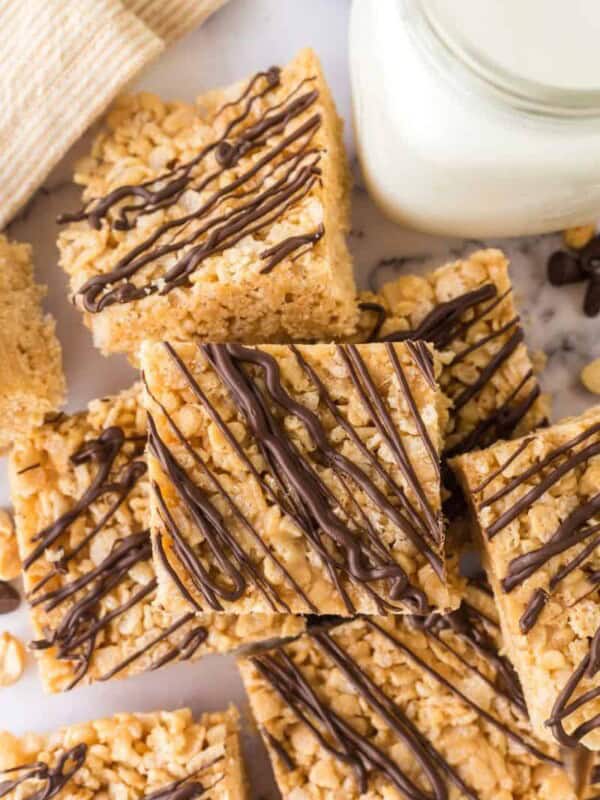 Rice Krispie Treat Squares made with peanut butter and chocolate drizzle with a glass of milk.