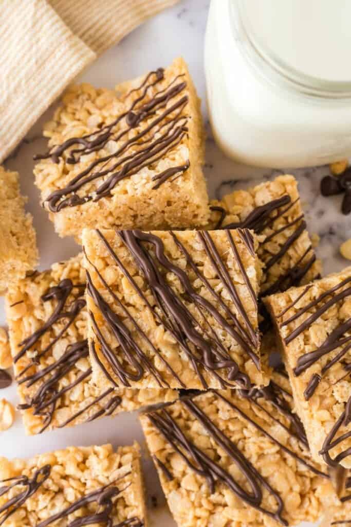 Rice Krispie Treat Squares made with peanut butter and chocolate drizzle with a glass of milk.