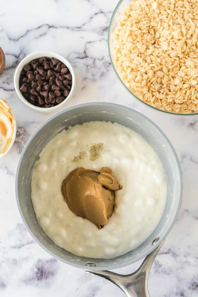 Adding peanut butter to butter and marshmallow mixture in small saucepan.