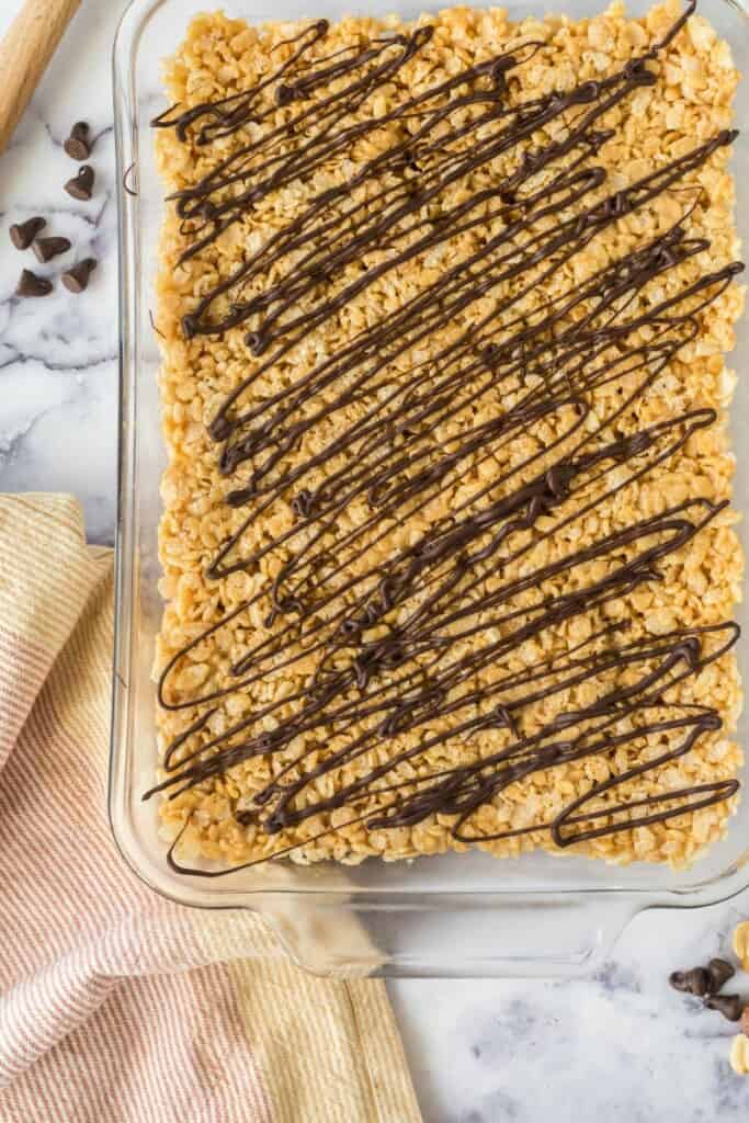 Close view of chocolate drizzled rice krispie treats in a clear baking dish.