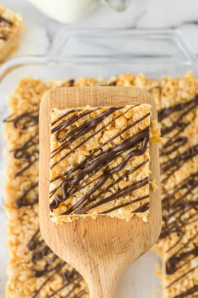 A close up view of a chocolate drizzled rice krispie treat on a wooden paddle.