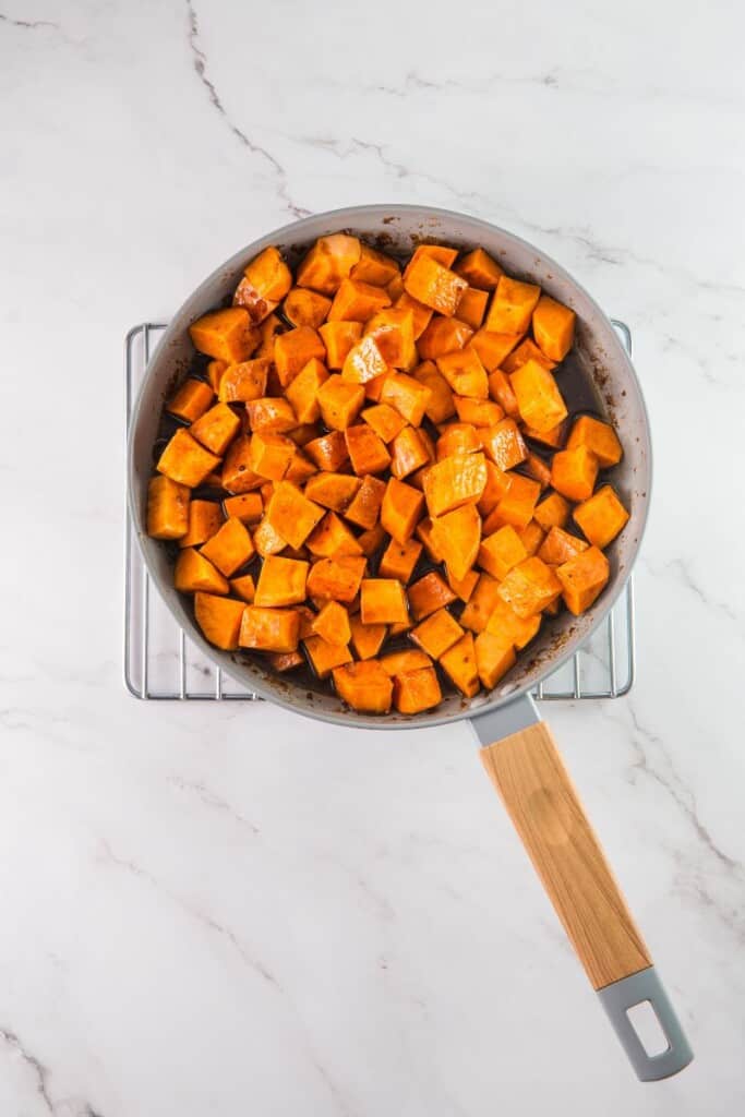 Adding cubed sweet potatoes to sugar mixture in saucepan.