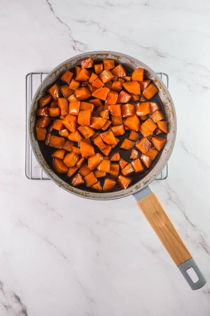 Cubed sweet potatoes coated in sugar mixture in a saucepan.