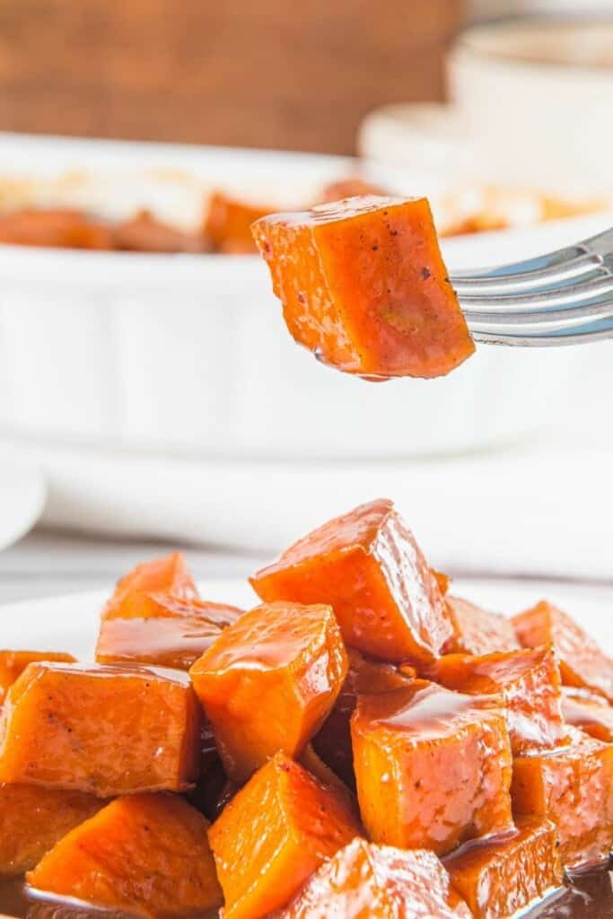 A fork holding a candied sweet potato cube over the serving dish of candied sweet potatoes.