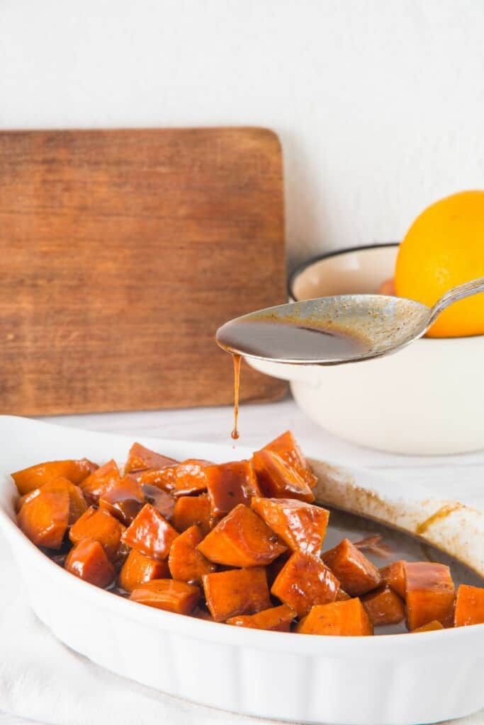 Candied sweet potatoes in a serving dish with a spoon drizzling sugar mixture on top.