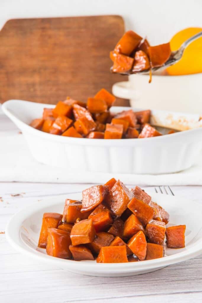 A plate of candied sweet potatoes with a spoon holding one bite above the plate.