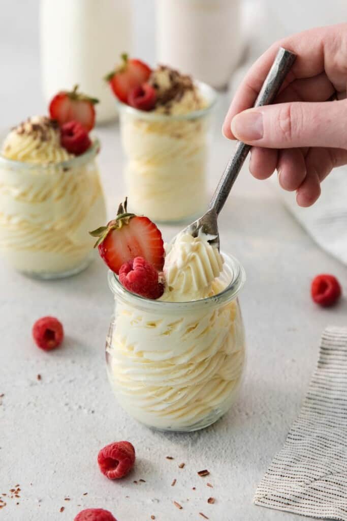 A spoon lifting a bite of vanilla mousse from a serving dish, topped with fresh strawberries.