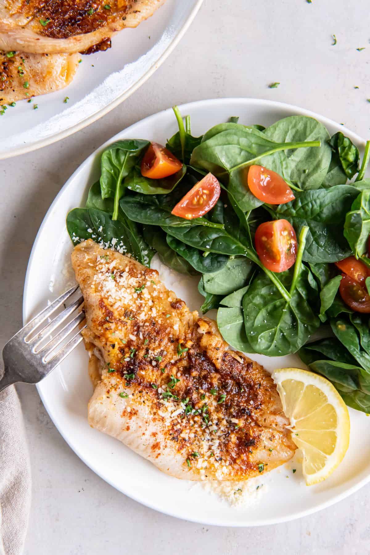 Air fryer flounder on a white plate served alongside a lemon wedge and salad.