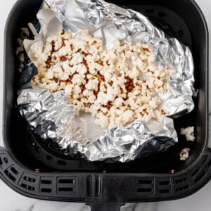 Popped popcorn in the air fryer basket with foil underneath.
