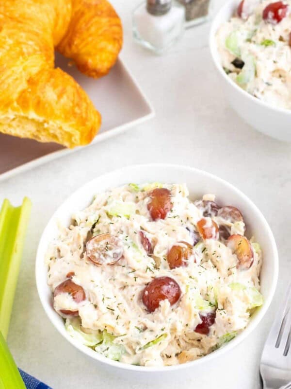 A bowl of chicken salad with a plate of croissants in the background.
