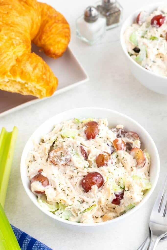 A bowl of chicken salad with a plate of croissants in the background.