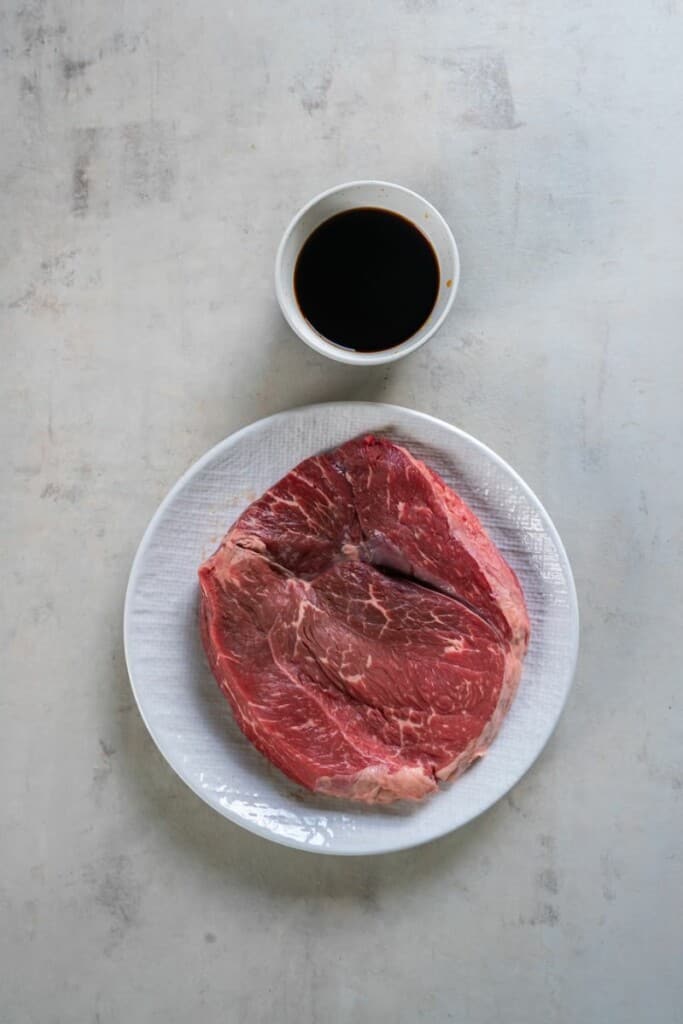 A plate with sirloin steak and a small bowl of teriyaki sauce.
