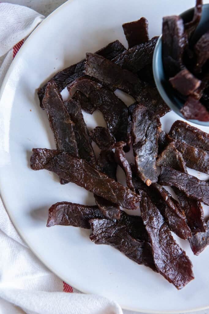 Close up view of beef jerky slices on a white plate.