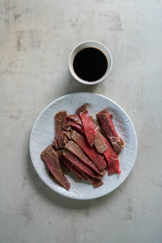 Sirloin steak cut into pieces on a white plate next to a small bowl of teriyaki sauce.