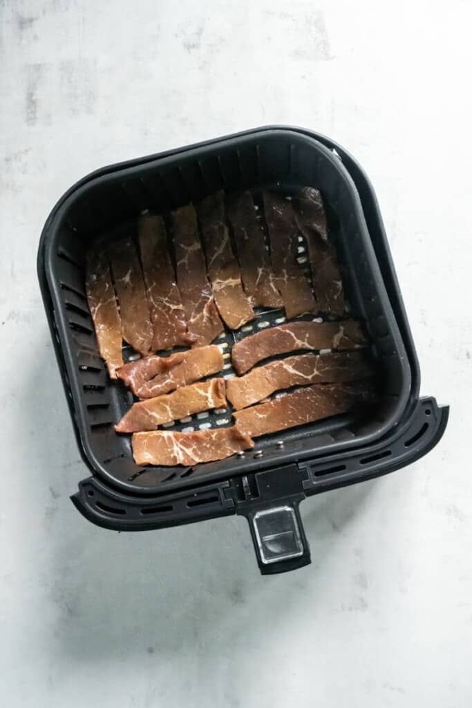 Sirloin steak pieces in a single layer of a black air fryer basket.