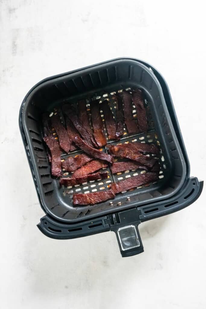 Sirloin beef jerky pieces resting in a single layer of a black air fryer basket.