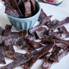 A plate holding beef jerky pieces and a small blue bowl holding additional pieces.