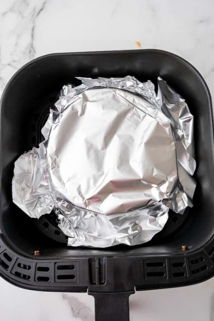 Aluminum foil covering homemade bread dough in a black air fryer basket.