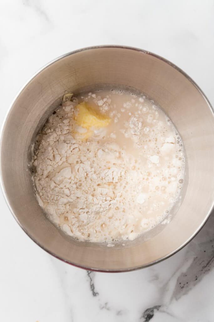 Adding flour, butter and salt to water mixture in a mixing bowl.
