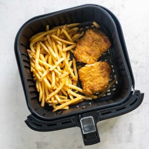 Two fish filets and chips resting in a black air fryer basket.
