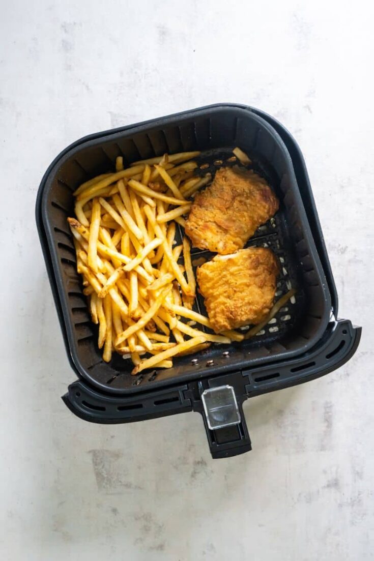 Two fish filets and chips resting in a black air fryer basket.