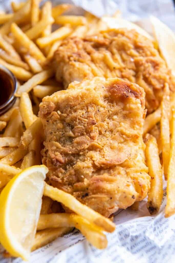 A close up view of a basket of fish and chips with lemon wedges and dipping sauce.