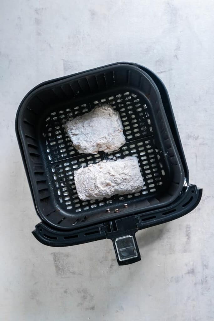 Two battered cod filets resting in a black air fryer basket.