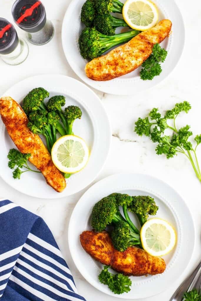 Overhead view of three plates of seasoned halibut with rice and broccoli.